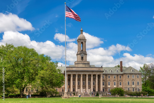 The Old Main building on the campus of Penn State University and American flag in spring sunny day, State College, Pennsylvania.
