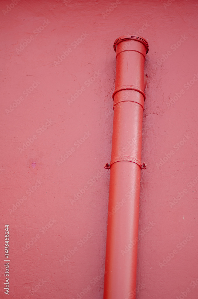 Minimalistic photo featuring a vertical red metal pipe attached to a pink painted wall, perfect for use in urban design, construction, or architectural projects. Minimalistic photo featuring a vertical red metal pipe attached to a pink painted wall, perfect for use in urban design, construction, or architectural projects.