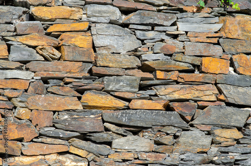 Closeup view of an old dry stone wall made from natural slate rocks, showing rough rustic texture and earthy colors. Perfect for architectural backgrounds or design projects.