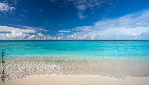 a serene beach with clear turquoise water gently meeting the sandy shore under a blue sky with clouds