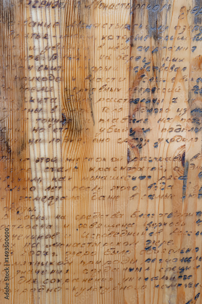 Fototapeta premium Close-up of a wooden panel featuring unrecognizable wood burn text in Russian language displaying texture and detail. Wood burning