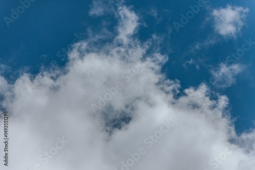 A clear blue sky bordered by soft, white cumulus clouds, creating a peaceful and open atmosphere with ample copy space.