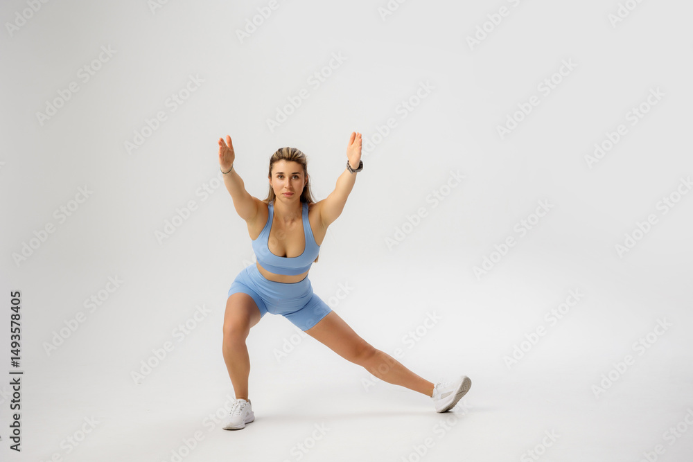 Fototapeta premium Fitness enthusiast performs lateral lunge exercise in a studio with light background and athletic attire