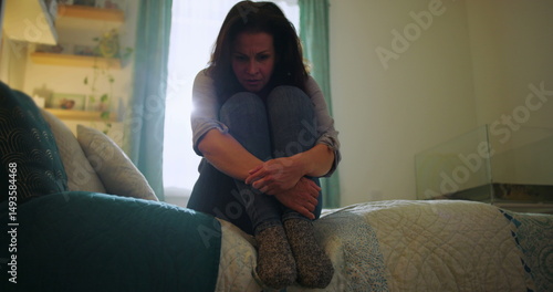 Фотография Woman sitting on bed, tightly clutching knees, crying in anguish, themes of desp