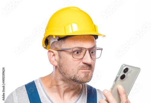 Rage repairman using the mobile phone, isolated on white background. Close up furious middle-aged construction worker looks to smartphone. Craftsman against white wall