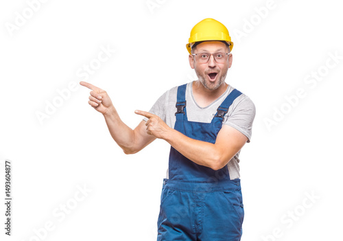 Surprised middle-aged construction worker while standing and pointing to blank space - copy space, promoter repairman with happy laugh, isolated on white background. Craftsman against white wall