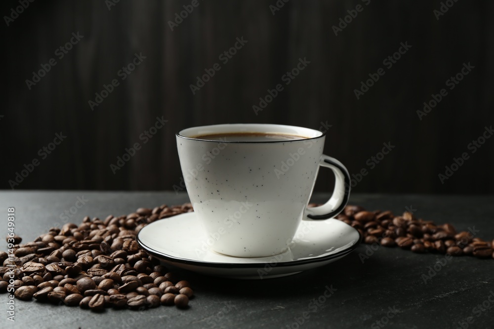 Fototapeta premium Aromatic coffee in cup and beans on black table, closeup