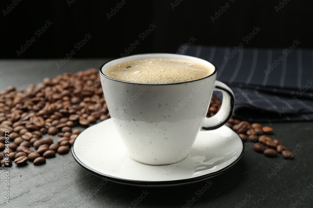 Obraz premium Aromatic coffee in cup and beans on black table, closeup