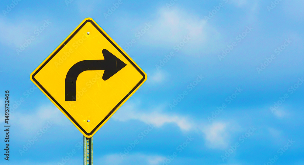 A yellow road sign with a right turn arrow against a blue sky with soft white clouds behind it A yellow road sign with a right turn arrow against a blue sky with soft white clouds behind it