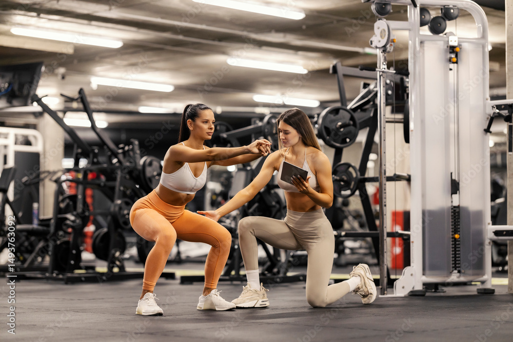 Obraz premium Sportswoman doing squats endurance while her personal trainer is helping her.