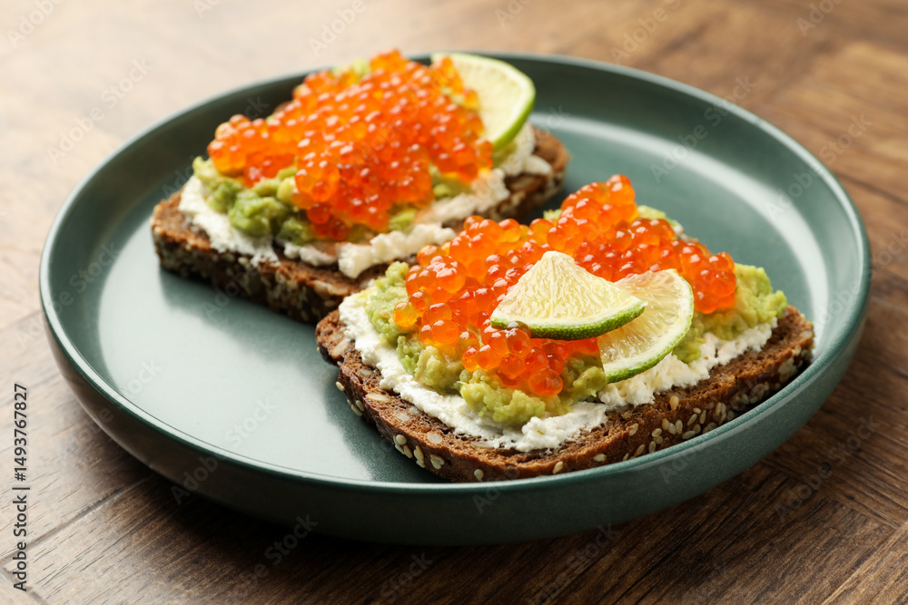 Delicious sandwiches with avocado, red caviar, cream cheese and lime on wooden table, closeup Delicious sandwiches with avocado, red caviar, cream cheese and lime on wooden table, closeup