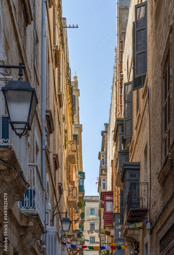 Fototapeta premium A view down an alleyway in Valletta old city, Malta, with traditional houses, bay windows and colourful shutters.