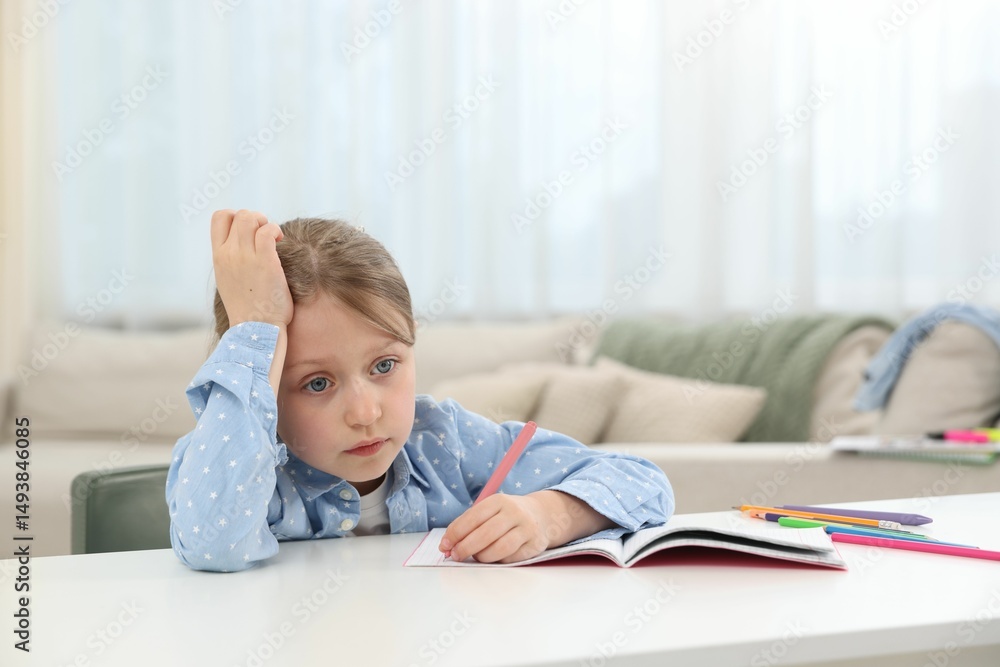 Tired little girl doing homework at table indoors Tired little girl doing homework at table indoors