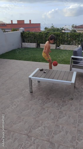 A boy in yellow shorts is playing with a basketball on a concrete floor