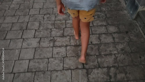 A child is walking barefoot on a brick sidewalk