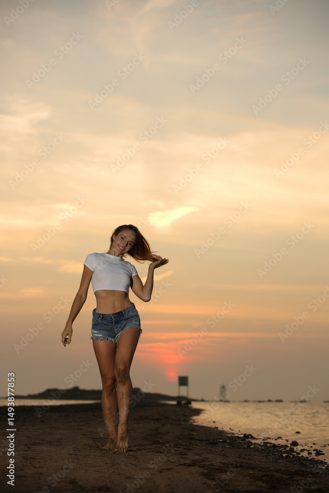 Fototapeta premium A beautiful young smiling blonde in a lacy white short top and u denim shorts