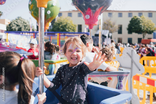 Little girl waving hand enjoying carousel ride at amusement park