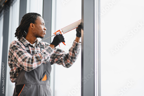 Slika na platnu African American Skilled worker sealing window for ventilation repair