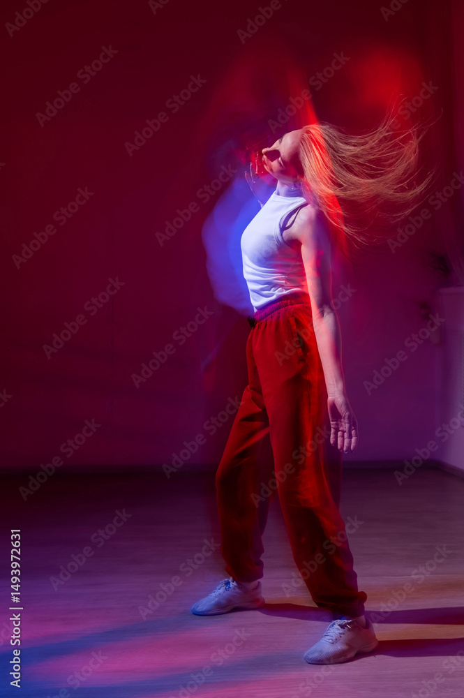 Fototapeta premium A young woman dances contemporary dances in blue and red light. Long exposure. Vertical photo.