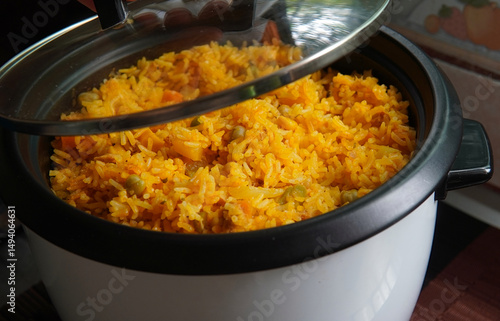 Hand lifting the lid of a rice cooker with yellow rice with tuna inside, typical Costa Rican food