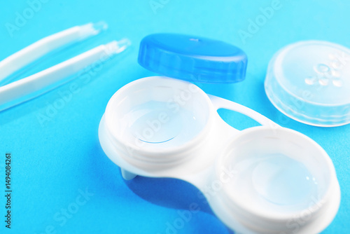 Contact lenses in case and tweezers on light blue background, closeup