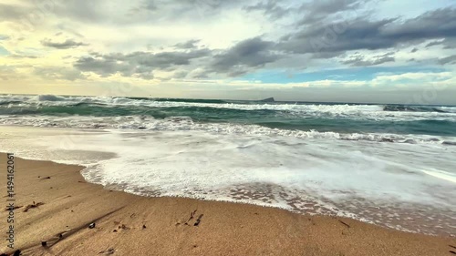 Experience the tranquility of serene beach waves gently rolling in beneath a dramatic and cloudy sky overhead