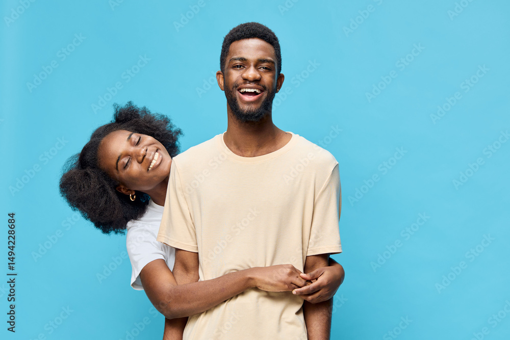 Obraz premium Happy young couple embracing each other against a bright blue background, showcasing love and joy with vibrant clothing and cheerful expressions