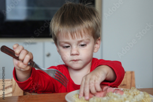 Tableau sur toile smiling toddler sitting at table with plate of noodles and sausage learning to u