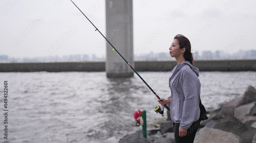 岩場に立ち海を眺める女性の釣り人 岩場に立ち海を眺める女性の釣り人