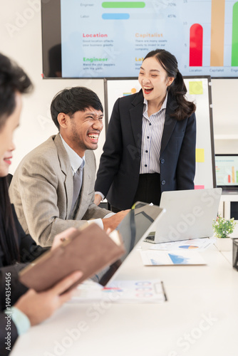 Asian business group discusses new project documents and presents in conference room, laughing and enjoying working together.