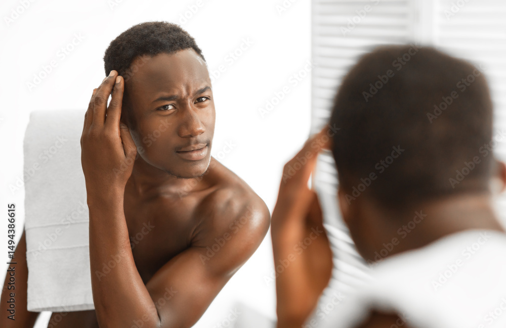 Obraz premium Dandruff Hair Problem. Black Man Looking In Mirror Examining Head Having Male-Pattern Baldness Issue Standing In Modern Bathroom Indoors. Men's Haircare Treatment Concept. Selective Focus
