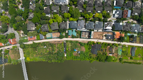 Top-down drone view of a narrow canal bordered by lush greenery and adjacent residential villas with gardens, illustrating Vietnam’s blend of waterways and suburban housing.