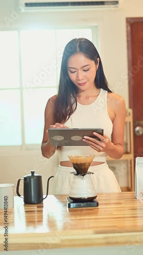 Happy asian woman using digital tablet while preparing pour over coffee at home