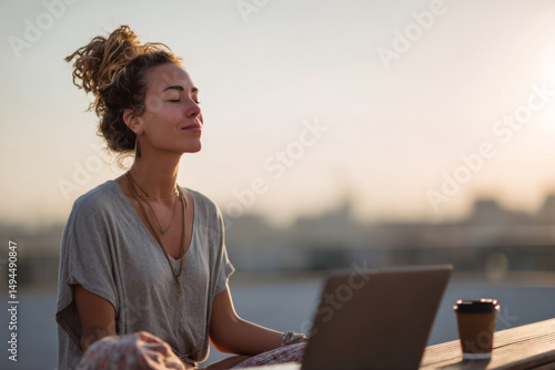 Young woman meditating outdoors at sunset with a laptop and coffee cup on a table. Great for wellness, digital detox, mindfulness, or remote work lifestyle concepts.