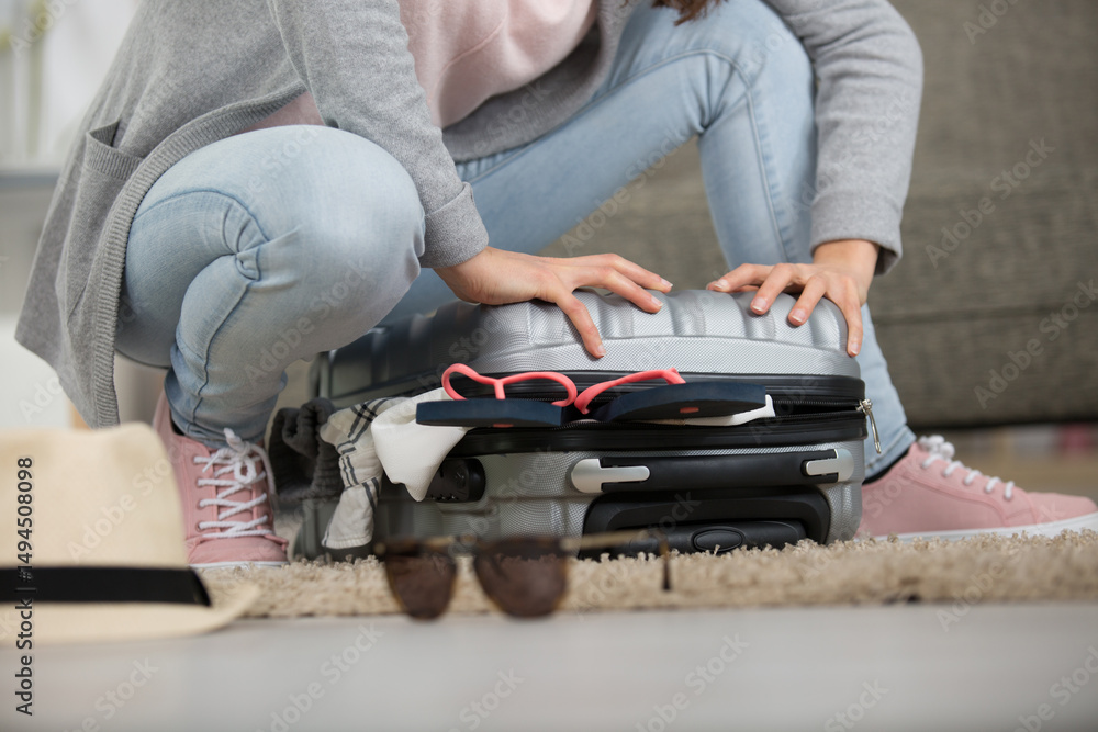 Fototapeta premium young woman standing on her knees on overfilled suitcase