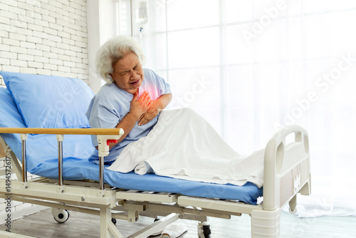 Elderly woman clutching chest in pain while sitting in a hospital bed, showing heart attack symptoms. Useful for healthcare, cardiology, emergency, and patient care microstock content.