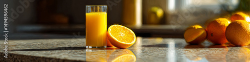 A glass of orange juice with sliced oranges on a reflective surface in a kitchen setting indoors