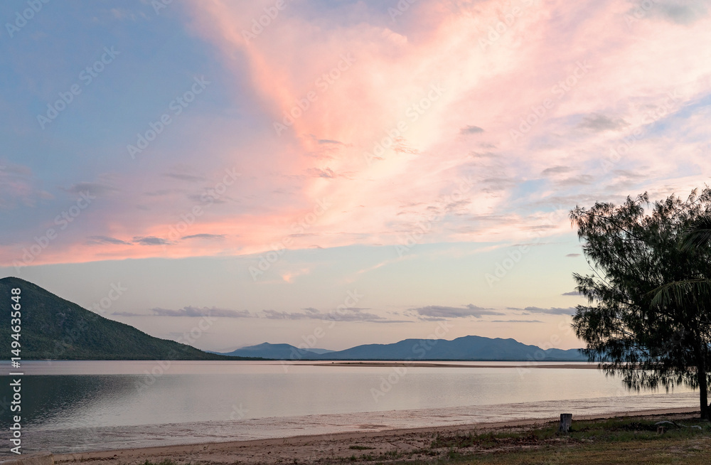 Fototapeta premium Soft pastel clouds streak across the sky at sunset over a calm shoreline.