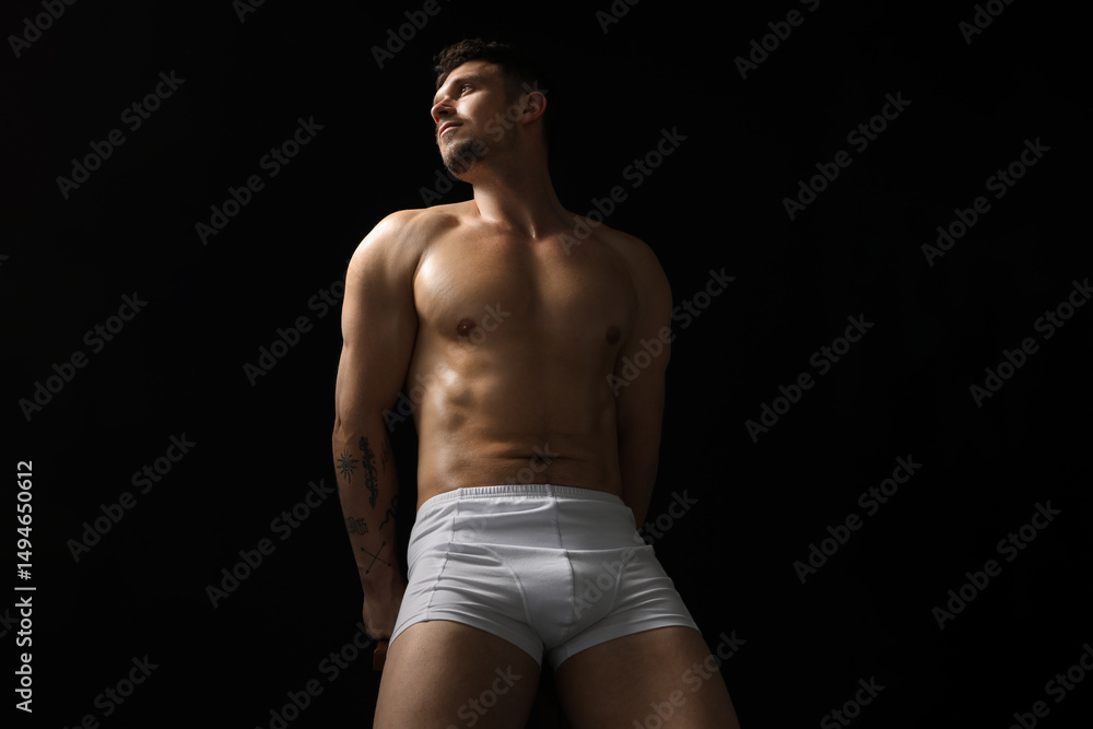 Fototapeta premium Young man in stylish white underwear on chair against black background, low angle view