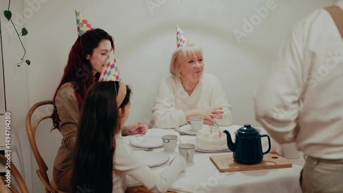 A family sits at a table and talks as a grandfather approaches them holding a knife, then they take the candles out of the cake