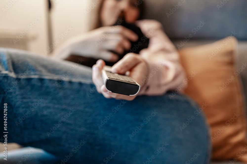 Obraz premium Woman relaxing on sofa holding remote control: overcoming anxiety and boredom