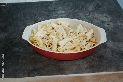 A red bowl of pasta with a white sauce. The pasta is in the shape of a tube