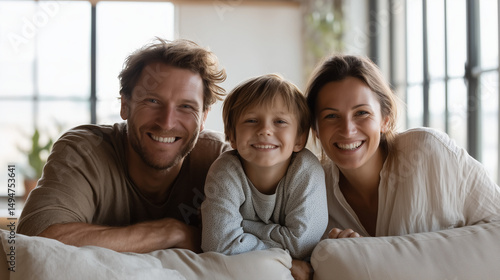 modern family (father, mother, young son) relaxing together on a minimalist beige sofa in a bright modern living room