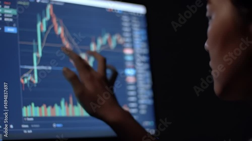 Individual analyzes stock trading charts on a computer screen in a dark environment. The focus is on insightful market trends and investment strategies.