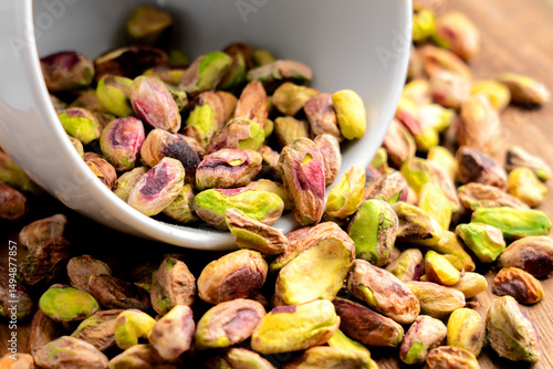 Peeled pistachio kernels in white cup are placed in pile of natural nutritious nuts. Macro shot