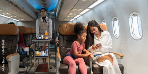 Quadro em tela Woman in white outfit and young girl in pink clothing enjoying on mobile phone together in airplane cabin