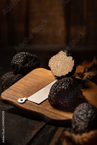 Premium food photography showing whole and sliced black truffles with a wooden truffle slicer on a dark rustic table. dramatic lighting highlights the rich texture and elegance of this rare gourmet