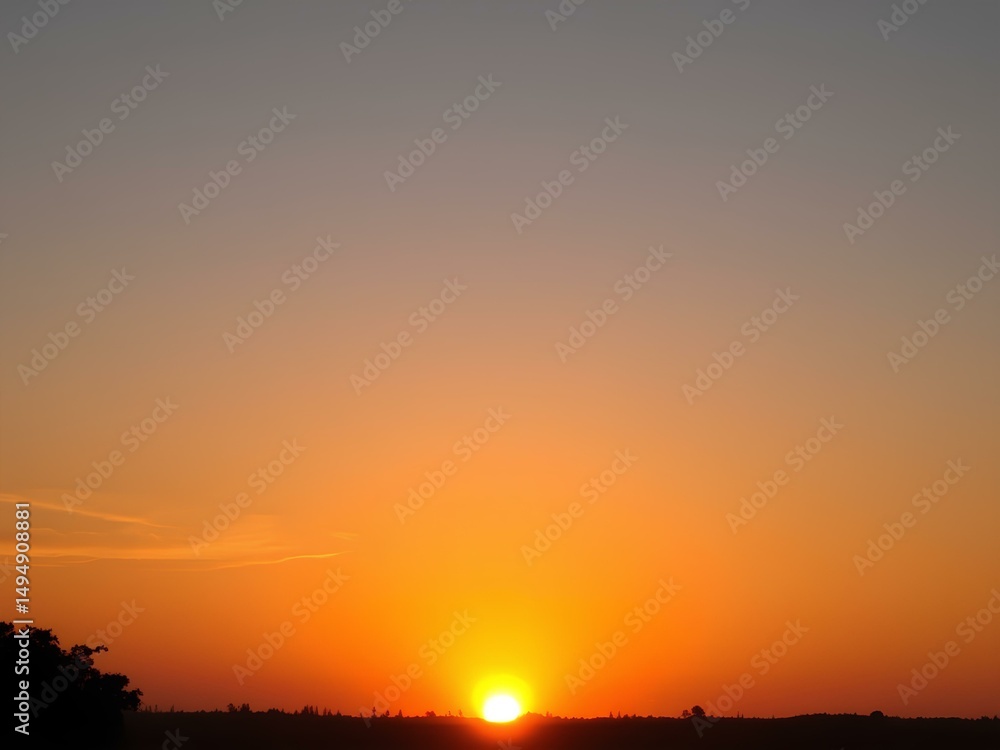 Naklejka premium Beautiful sunrise scene with the sun just above the horizon, casting warm orange and yellow hues across the sky and landscape