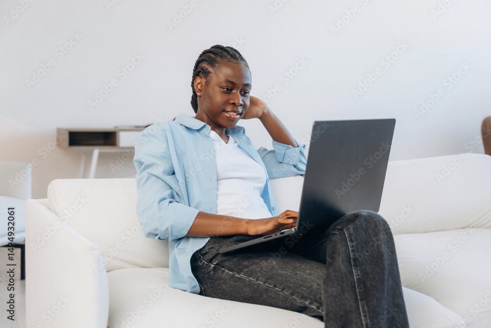 Naklejka premium Working by using laptop, sitting on sofa. Woman is at home in domestic room