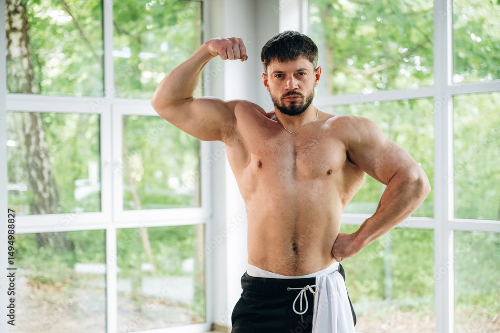 Fototapeta premium Shows the muscles. Shirtless strong man is standing against panoramic windows